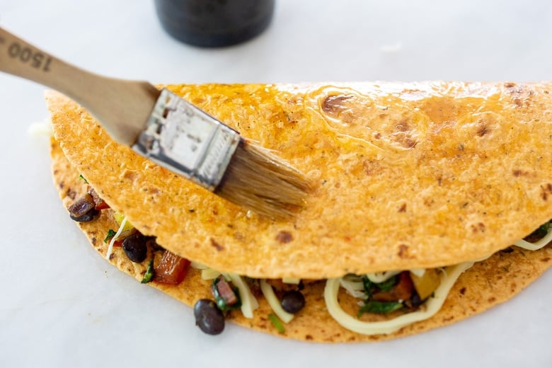 folded and filled tortilla being brushed with olive oil. 