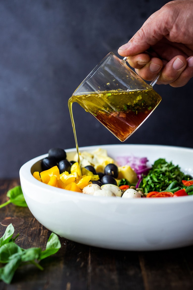 Pouring the Antipasto Salad Dressing over the salad