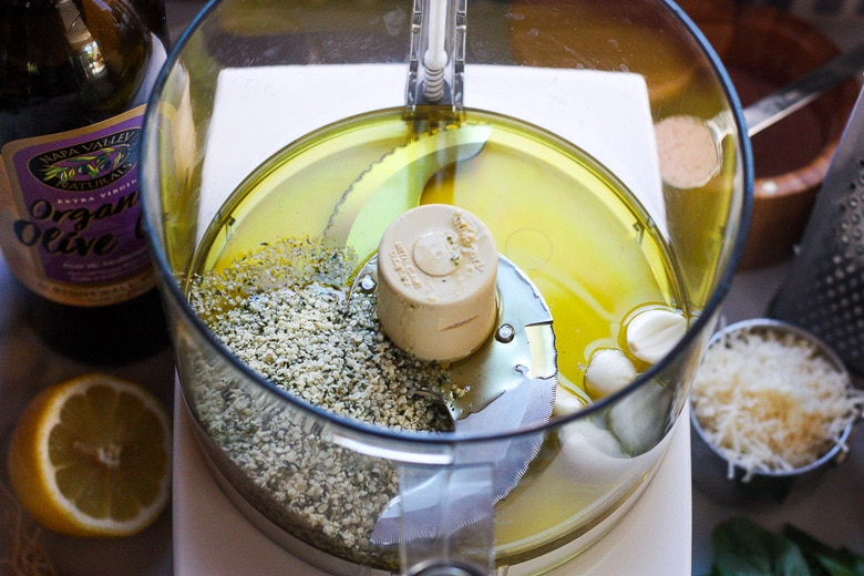 Food processor with olive oil, garlic and hemp seeds for making basil pesto.