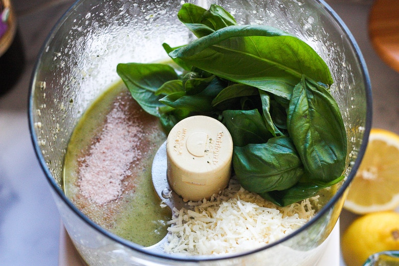 Adding basil, salt and cheese into the food processor for basil pesto. 