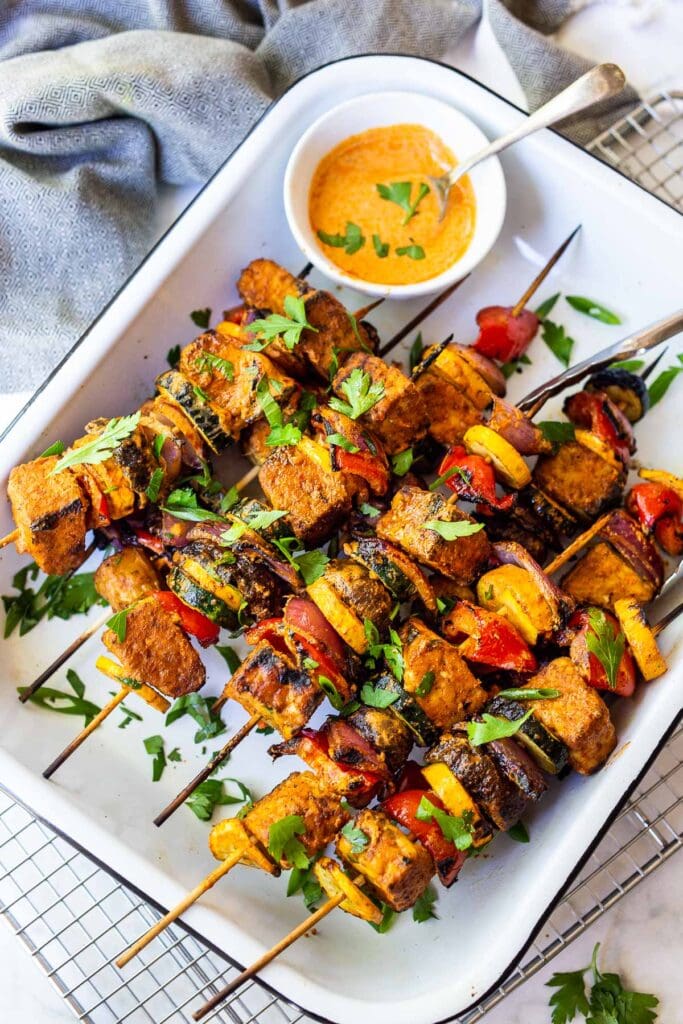 Moroccan grilled veggie skewers on a serving platter with tofu and a harissa yogurt marinade, topped with fresh herbs.