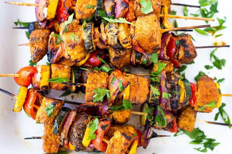 grilled veggie kabobs with harissa yogurt on a platter, scattered with fresh herbs