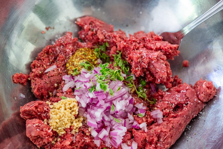 ground bison in a bowl with onion, garlic , mustard, thyme, salt and pepper 