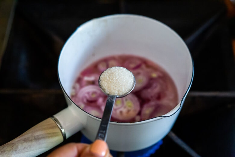 Putting sugar in the pan with the shallots for Pickled Shallots.
