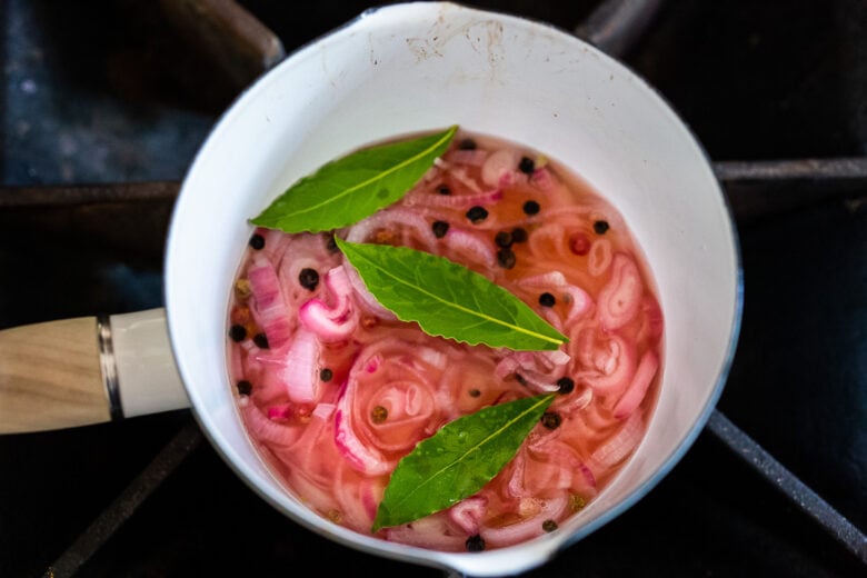 Adding bay leaves to the pickled shallots.