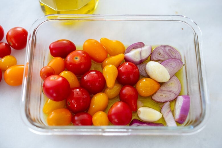 Tomatoes, garlic and shallot in a glass roasting pan for Tomato Vinaigrette.