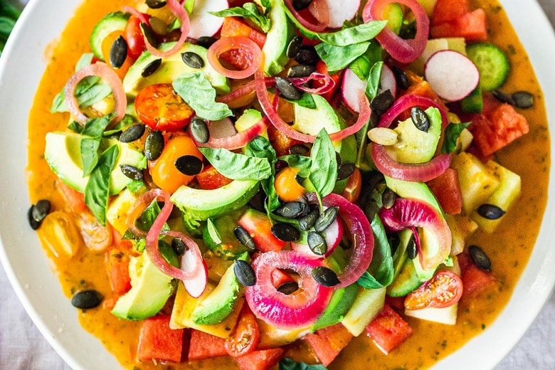 tomato watermelon salad on a plate with cucumber, avocado, radish, pickled shallots, 