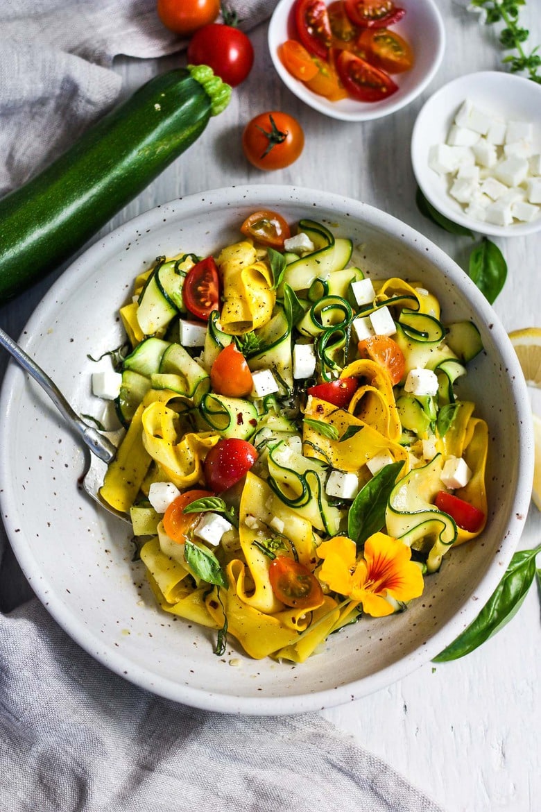 zucchini ribbons with feta and cherry tomatoes, garnished with fresh basil in bowl with fork.