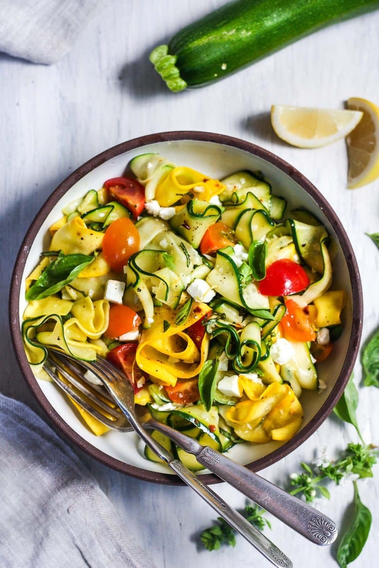 pasta bowl with zucchini ribbons with cherry tomatoes, fresh basil, feta, and forks.