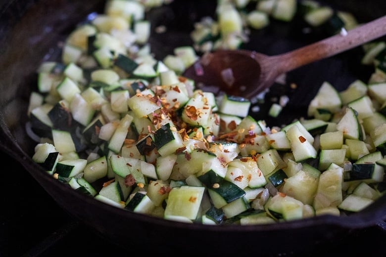 zucchini sautéing in a pan with chili flakes added.