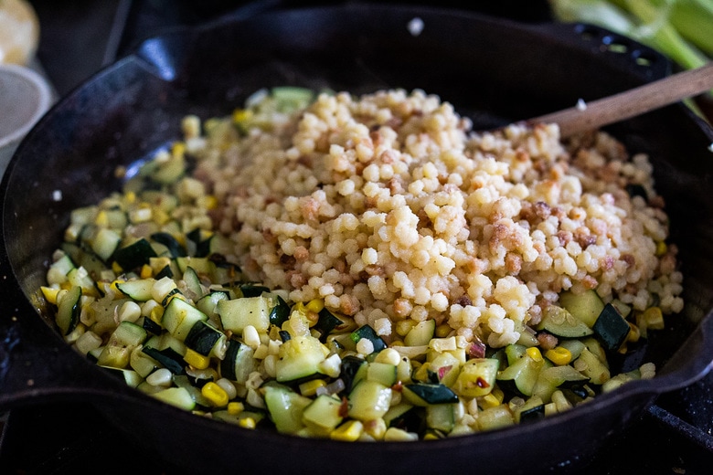 fregola being added to the pan with the zucchini and corn