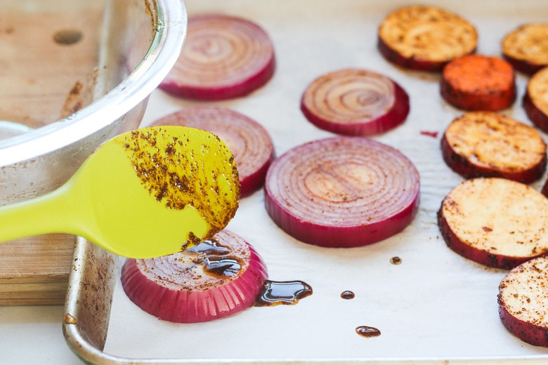 adding extra marinade to veggies on a sheet pan.