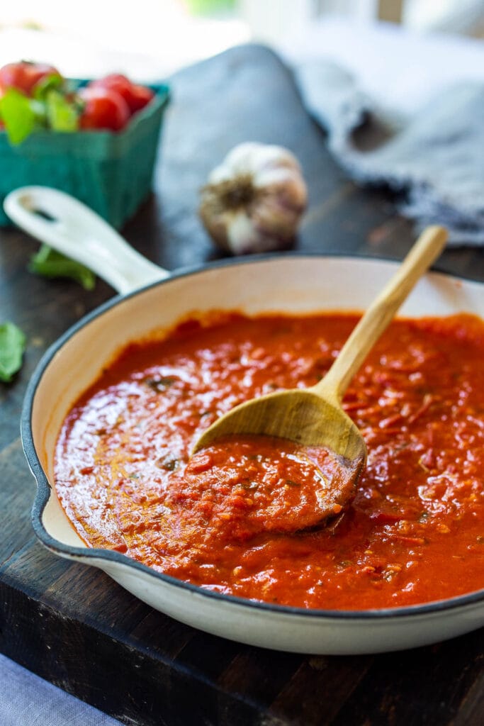 pan of marinara sauce with wood spoon lifting up some of the sauce.
