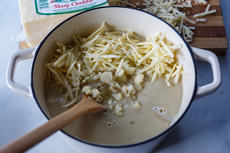 adding sharp cheddar cheese to the soup pot with creamy cauliflower soup.