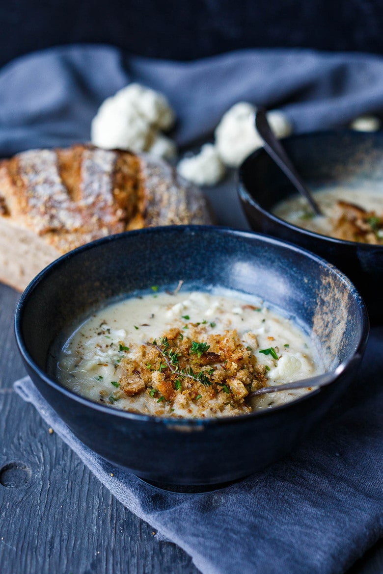 cauliflower cheddar soup in bowl with bread crumb topping and fresh thyme.