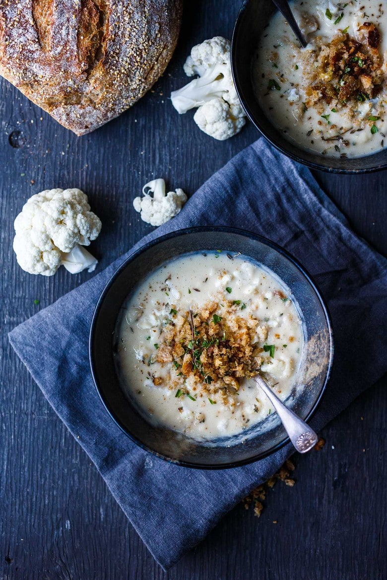 overhead of cauliflower cheddar soup in bowls with bread crumb topping and fresh herbs.