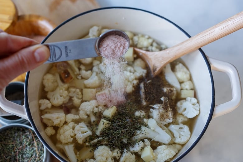 adding ingredients for cauliflower cheddar soup to pot- adding salt.
