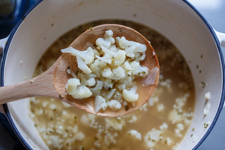 cooked cauliflower held up in wooden spoon over soup pot.