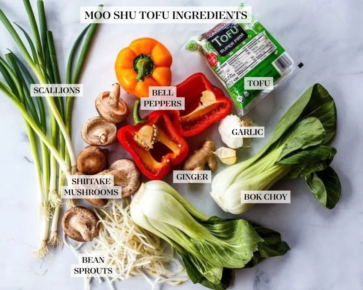 moo shu tofu ingredients on the counter, labeled - tofu, garlic, ginger, bok choy, bean sprouts, shiitake mushrooms, bell peppers, and scallions.