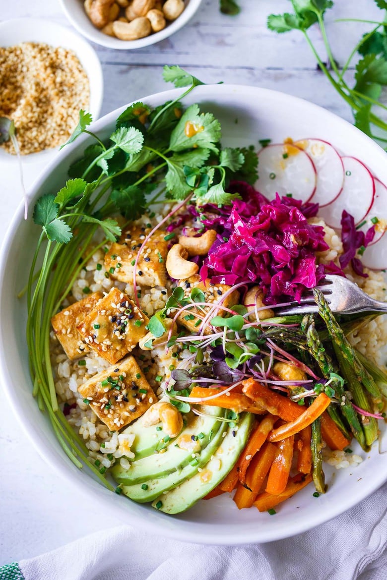 A delicious recipe for Miso Tofu and Veggies baked on a sheet pan in the oven, served over rice, with avocado, cashews radishes and flavorful miso dressing.