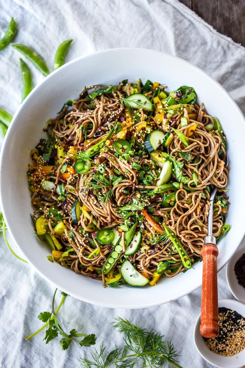 soba noodle salad mixed together in large bowl with cucumbers, peppers, jalapeños, herbs, snow peas, sesame seeds.