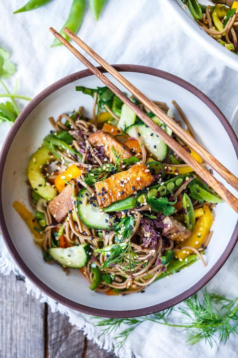 soba noodle salad in bowl topped with baked tofu, garnished with herbs and sesame seeds. 