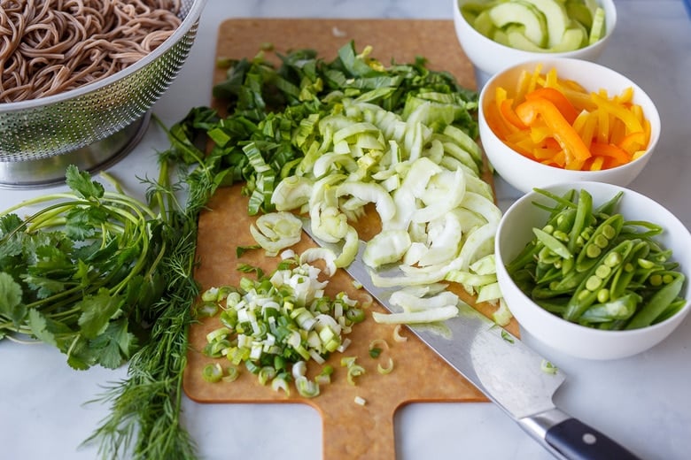 chopped veggies on cutting board with knife- bowls of snow peas, bell pepper, cucumber.