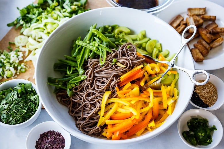 tossing salad together with all ingredients in bowl with noodles. 