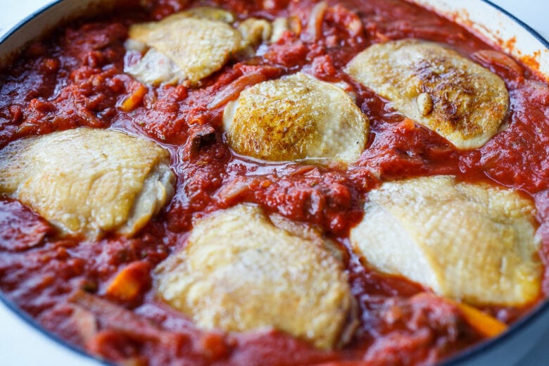 Adding chicken to sauce in chicken cacciatore.