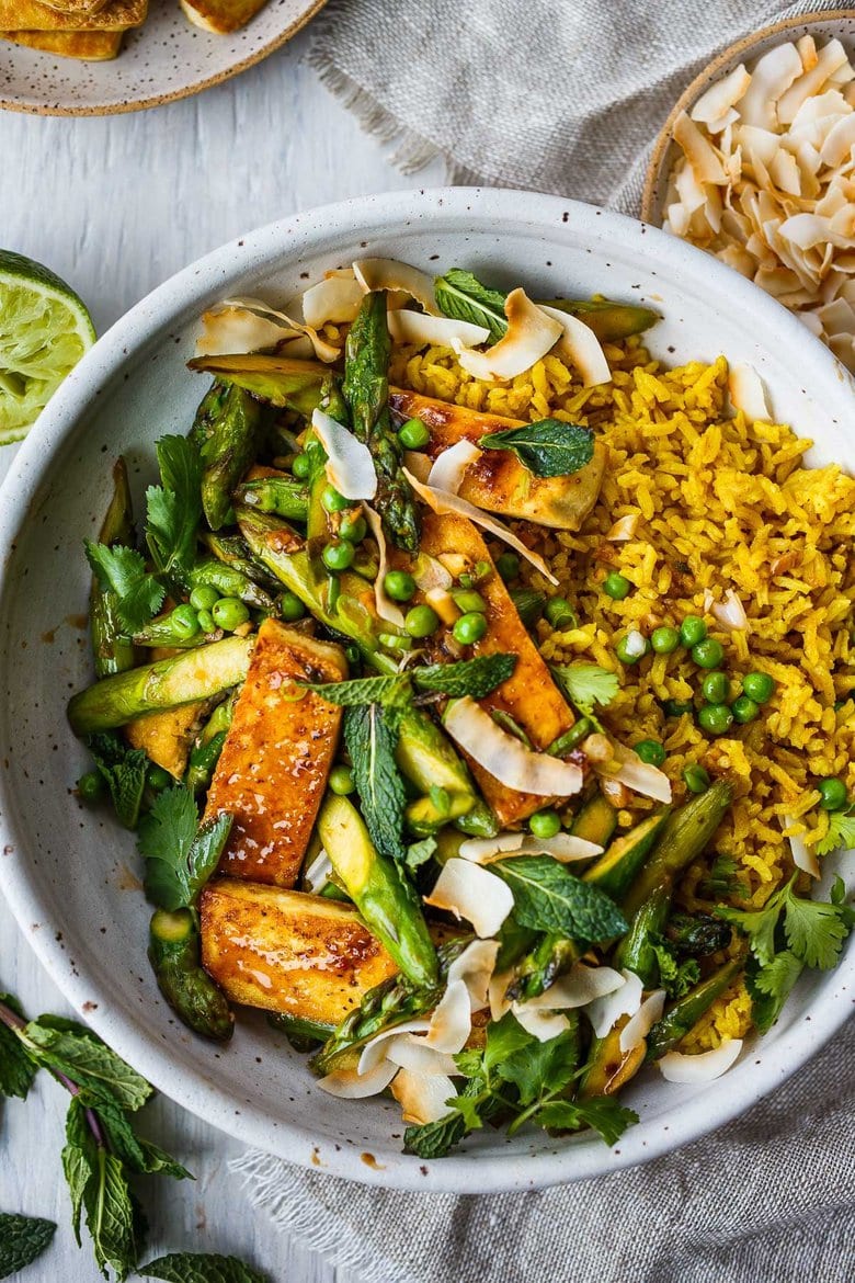 Delicious Coconut Rice Bowl is healthy and adaptable!  Curried jasmine rice cooked in coconut milk and topped with tofu or your choice of protein and seasonal vegetables.  All tossed with a simple, flavorful sauce, fresh cilantro, mint and toasted coconut flakes.
