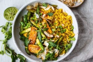 Delicious Coconut Rice Bowl is healthy and adaptable!  Curried jasmine rice cooked in coconut milk and topped with tofu or your choice of protein and seasonal vegetables.  All tossed with a simple, flavorful sauce, fresh cilantro, mint and toasted coconut flakes.