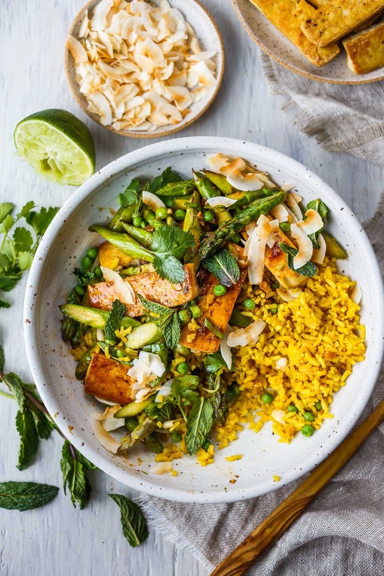 Delicious Coconut Rice Bowl is healthy and adaptable!  Curried jasmine rice cooked in coconut milk and topped with tofu or your choice of protein and seasonal vegetables.  All tossed with a simple, flavorful sauce, fresh cilantro, mint and toasted coconut flakes.