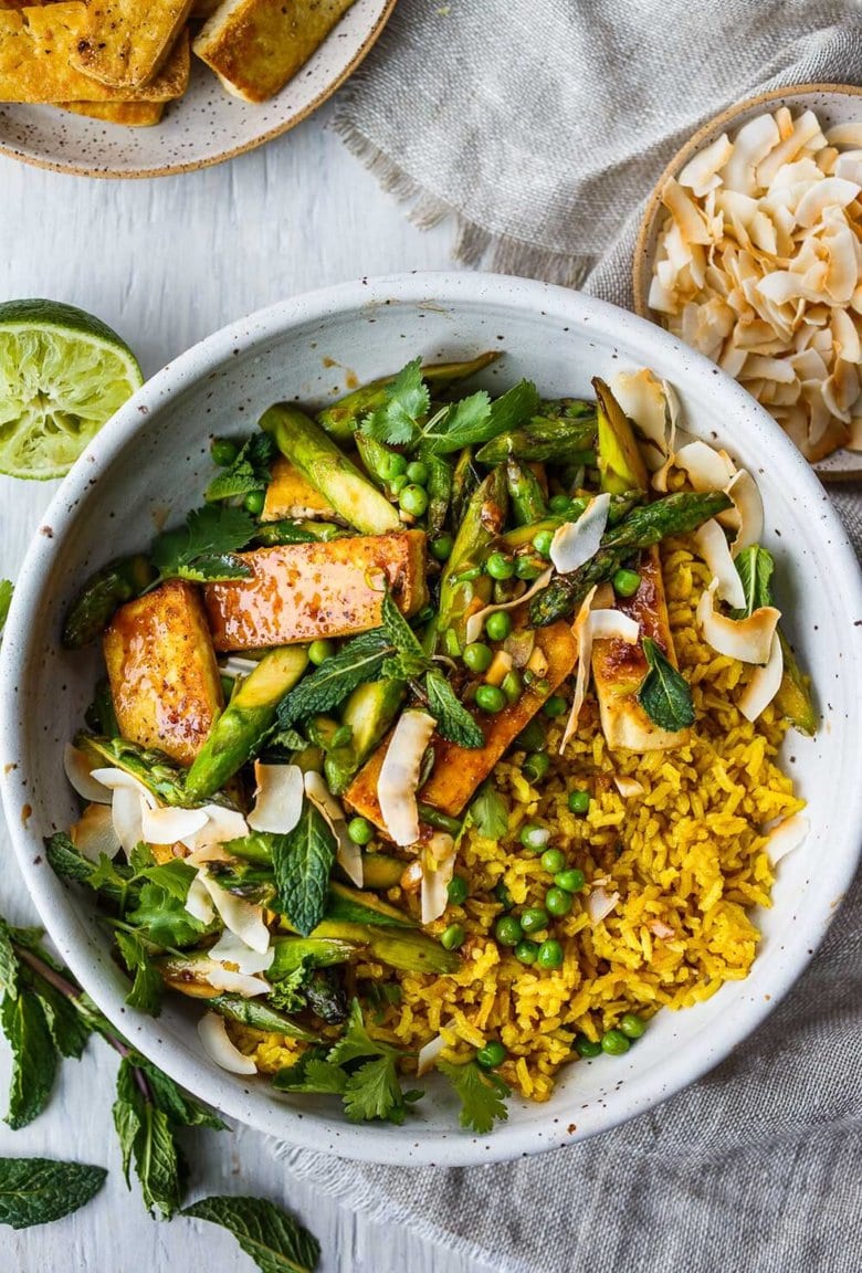 Delicious Coconut Rice Bowl is healthy and adaptable!  Curried jasmine rice cooked in coconut milk and topped with tofu or your choice of protein and seasonal vegetables.  All tossed with a simple, flavorful sauce, fresh cilantro, mint and toasted coconut flakes.
