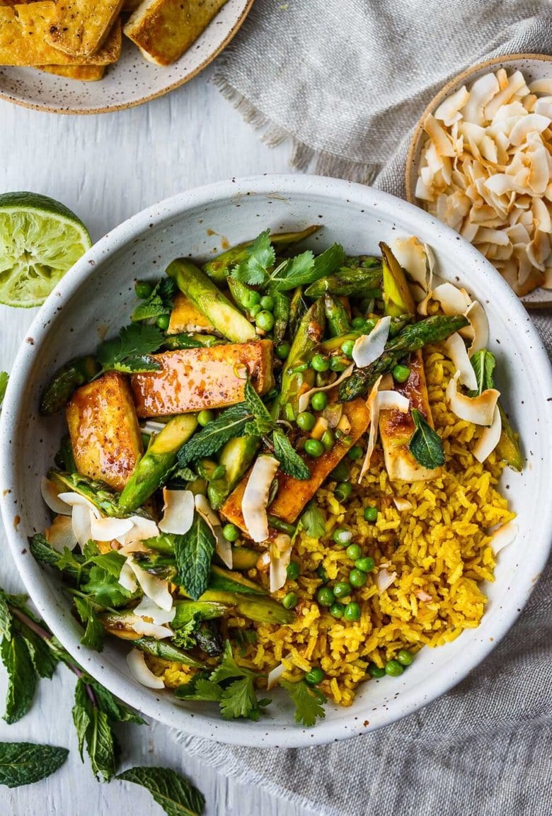 Delicious Coconut Rice Bowl is healthy and adaptable! Curried jasmine rice cooked in coconut milk and topped with tofu or your choice of protein and seasonal vegetables. All tossed with a simple, flavorful sauce, fresh cilantro, mint and toasted coconut flakes.