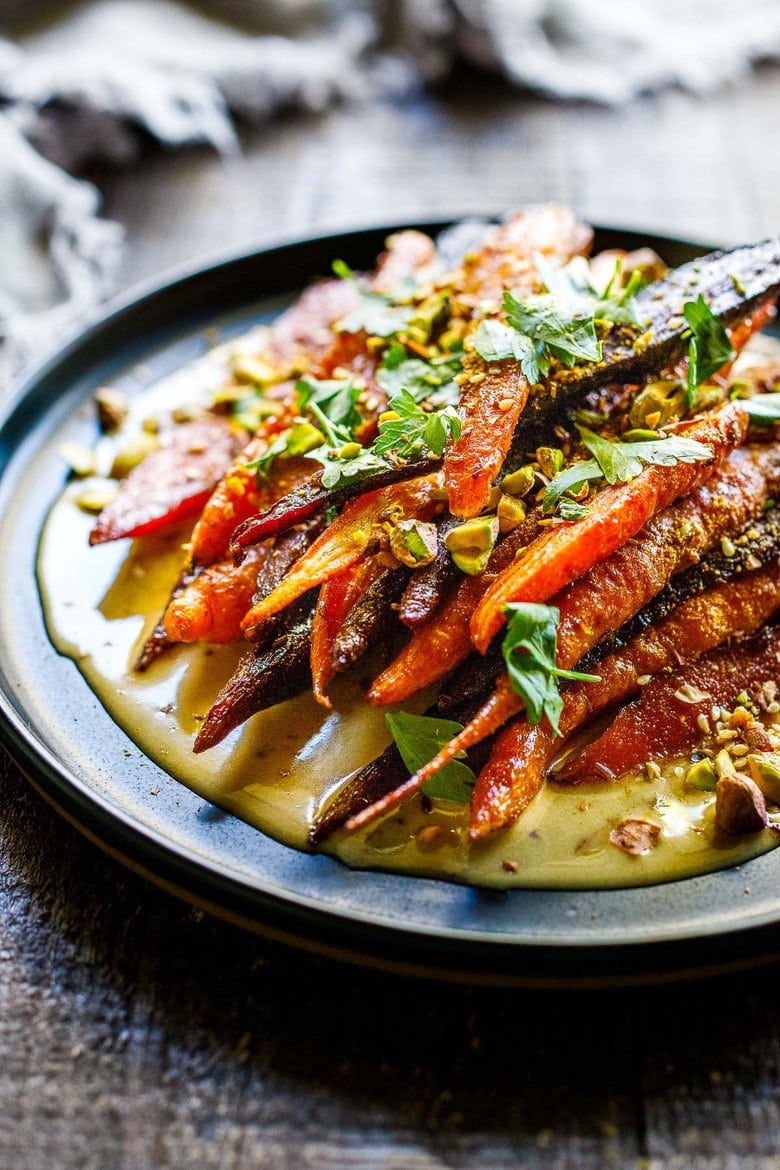 A quick and easy recipe for Roasted Carrots with cumin and coriander seeds, over a creamy Maple-Tahini Sauce, sprinkled with Pistachios, Dukkah and Aleppo chili flakes- a tasty vegan side dish that pairs with many things. 