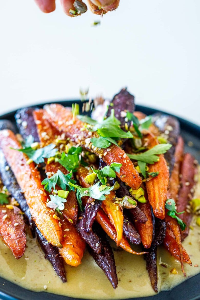 A quick and easy recipe for Roasted Carrots with cumin and coriander seeds, over a creamy Maple-Tahini Sauce, sprinkled with Pistachios, Dukkah and Aleppo chili flakes- a tasty vegan side dish that pairs with many things. 