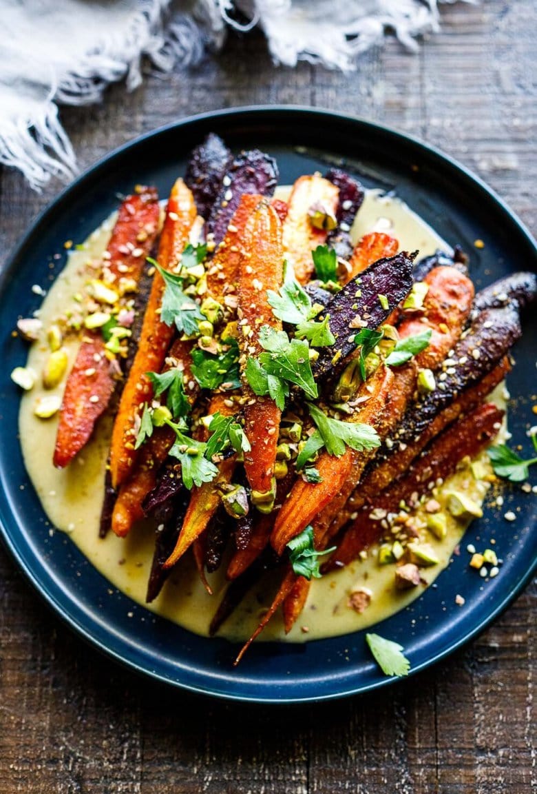 A quick and easy recipe for Roasted Carrots with cumin and coriander seeds, over a creamy Maple-Tahini Sauce, sprinkled with Pistachios and Dukkha, a tasty vegan side dish that pairs with many things.