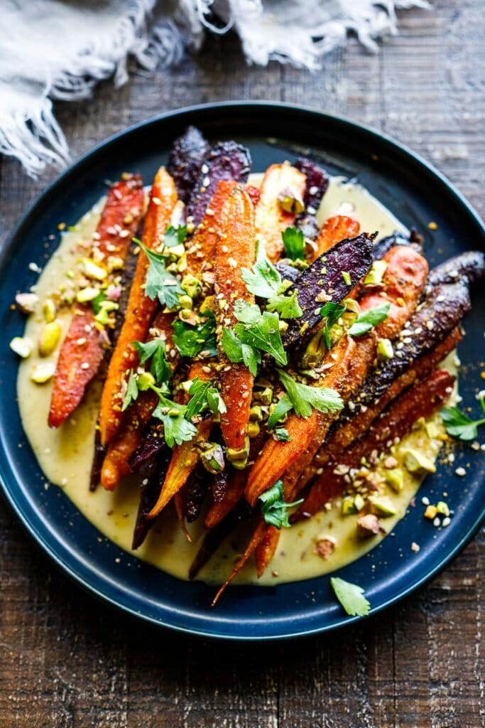 A quick and easy recipe for Roasted Carrots with cumin and coriander seeds, over a creamy Maple-Tahini Sauce, sprinkled with Pistachios and Dukkha, a tasty vegan side dish that pairs with many things.