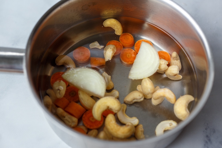 saucepan with cashews, carrots, onion slice, and water.