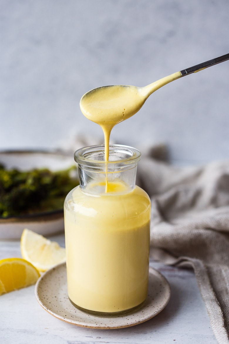 spoon dripping vegan hollandaise sauce into glass jar.