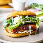 Blackened Salmon Sandwich! A succulent crispy crusted, cajun spiced, salmon fillet tucked into a toasted bun with fresh greens, cucumber, red onion, drizzled with creamy Dilly Ranch Dressing.