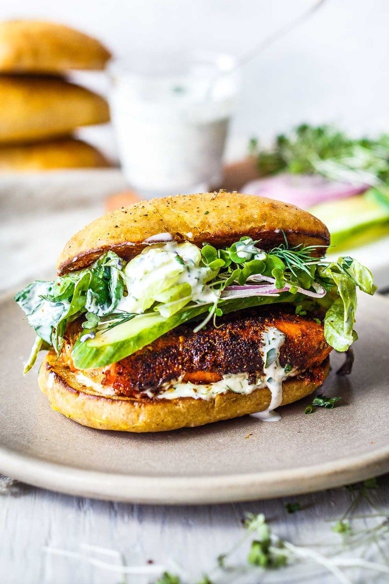 Blackened Salmon Sandwich!  A succulent crispy crusted, cajun spiced, salmon fillet tucked into a toasted bun with fresh greens, cucumber, red onion, drizzled with creamy Dilly Ranch Dressing.