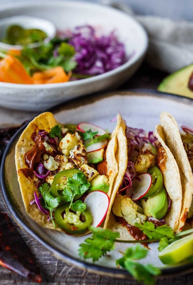 Roasted Cauliflower Tacos with quick and easy Mole Rojo sauce!  These healthy vegan tacos are loaded up with cabbage, avocado, radishes and cilantro and full of satisfying flavor and fresh crunchy ingredients.