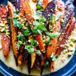 A quick and easy recipe for Roasted Carrots with cumin and coriander seeds, over a creamy Maple-Tahini Sauce, sprinkled with Pistachios and Dukkha, a tasty vegan side dish that pairs with many things.