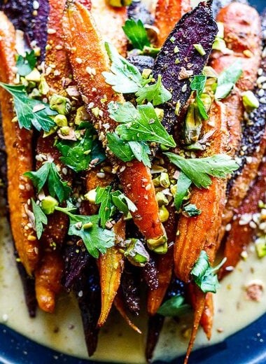 A quick and easy recipe for Roasted Carrots with cumin and coriander seeds, over a creamy Maple-Tahini Sauce, sprinkled with Pistachios and Dukkha, a tasty vegan side dish that pairs with many things. 