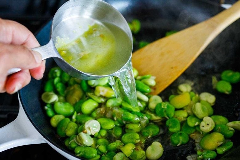 adding broth and fava beans to the skillet. 