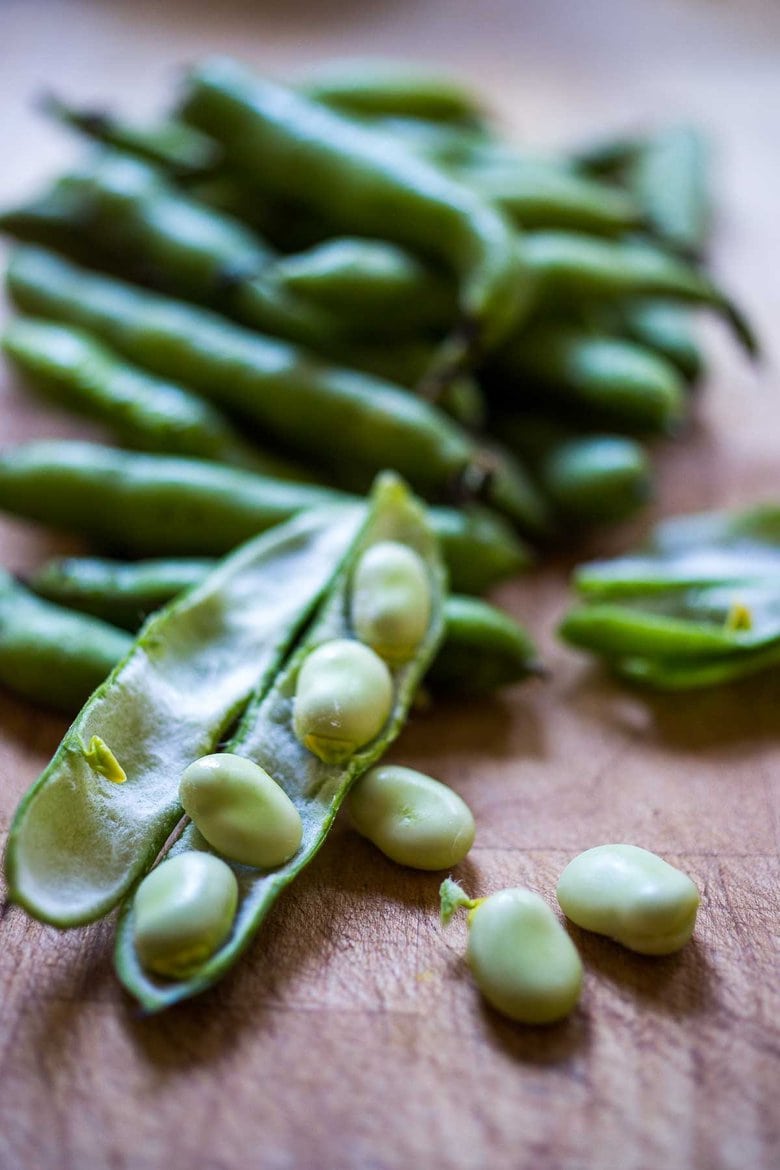 fava bean pods being split open with beans showing
