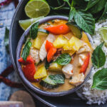 pineapple curry in a circular bowl garnish with basil and lime wedges