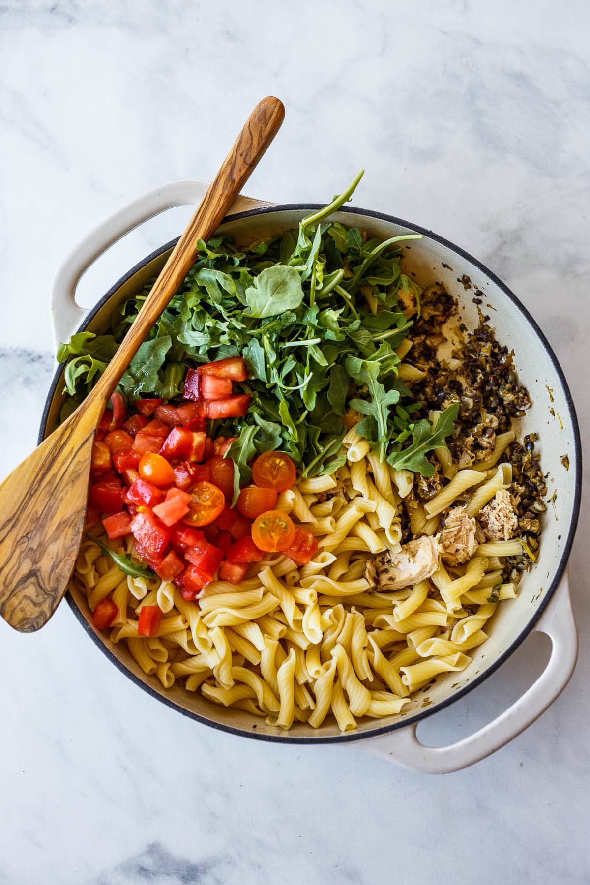mixing pasta with tomatoes, tuna, olive tapenade and arugula