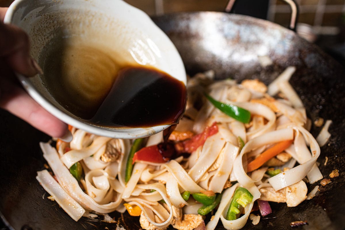 pouring sauce over rice noodles in a wok